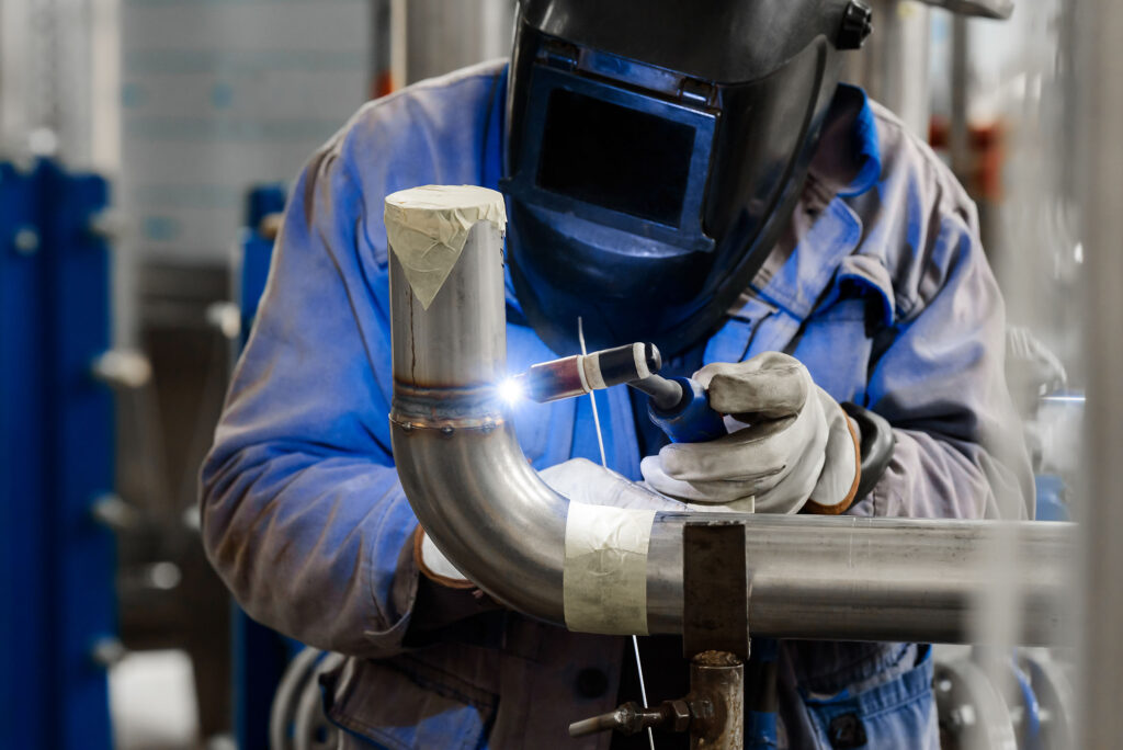 Male in face mask welds with argon arc welding pipes.